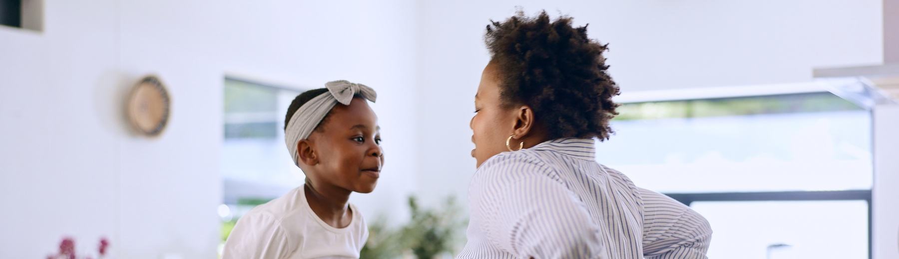 A mother and her daughter talk face to face in the kitchen, the girl sitting on the counter