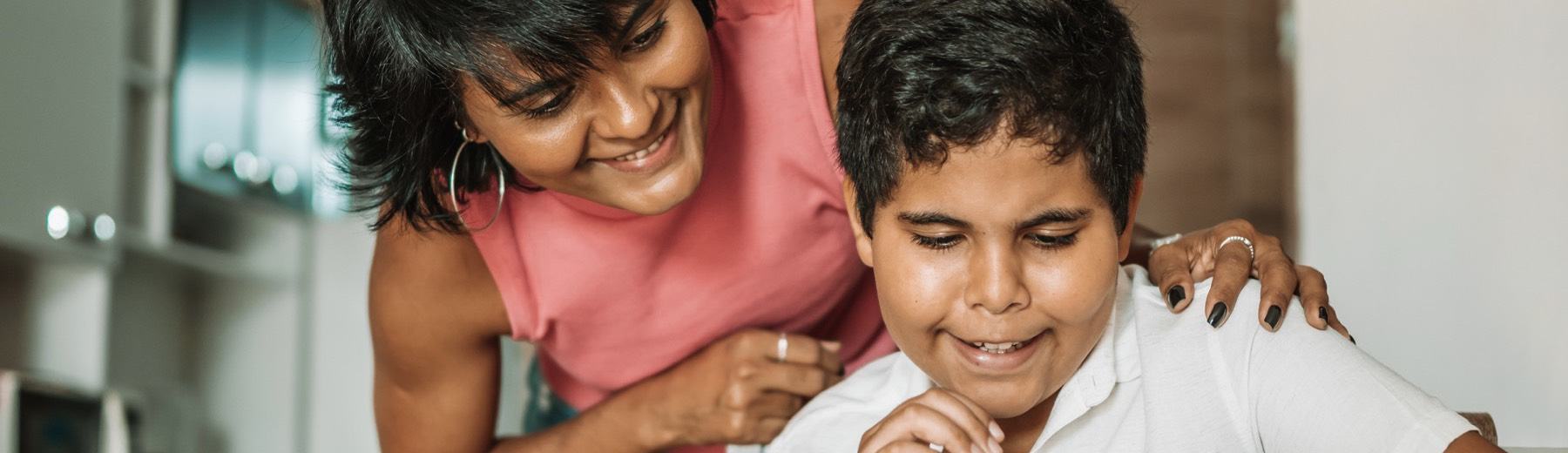 A mother leans over her son's shoulder as he draws at the kitchen table